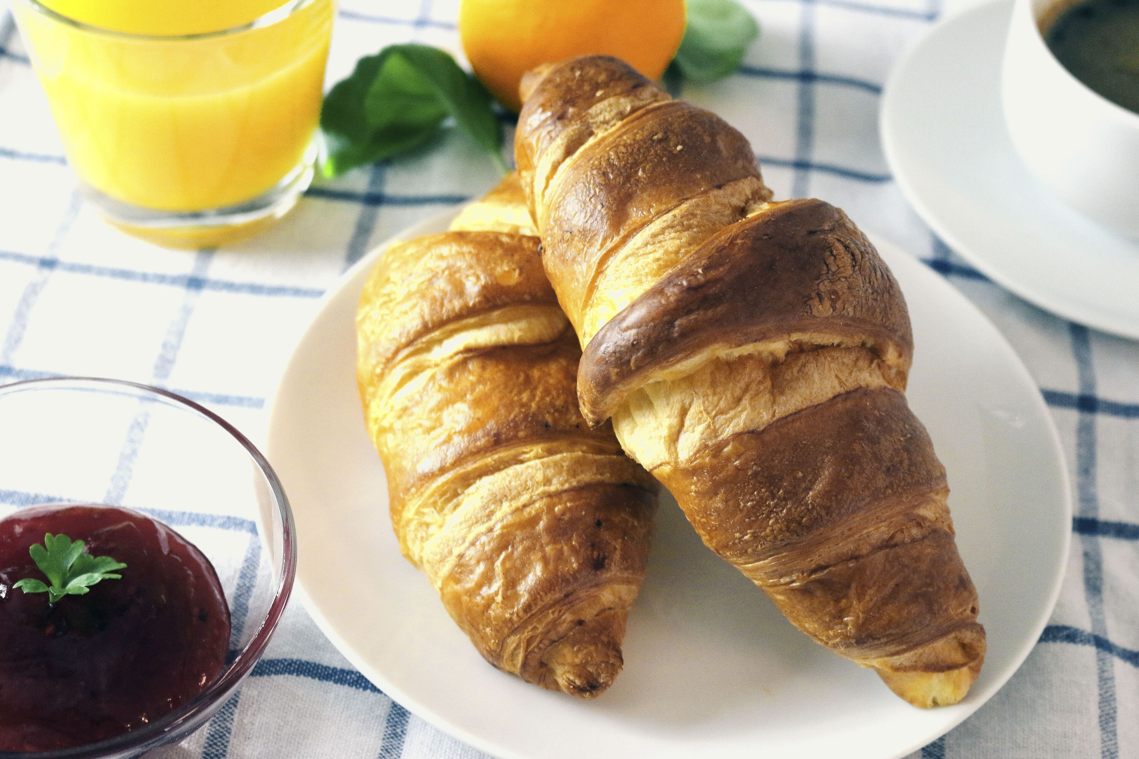 Two croissants on a white plate with a glass of orange juice and a bowl of jam.