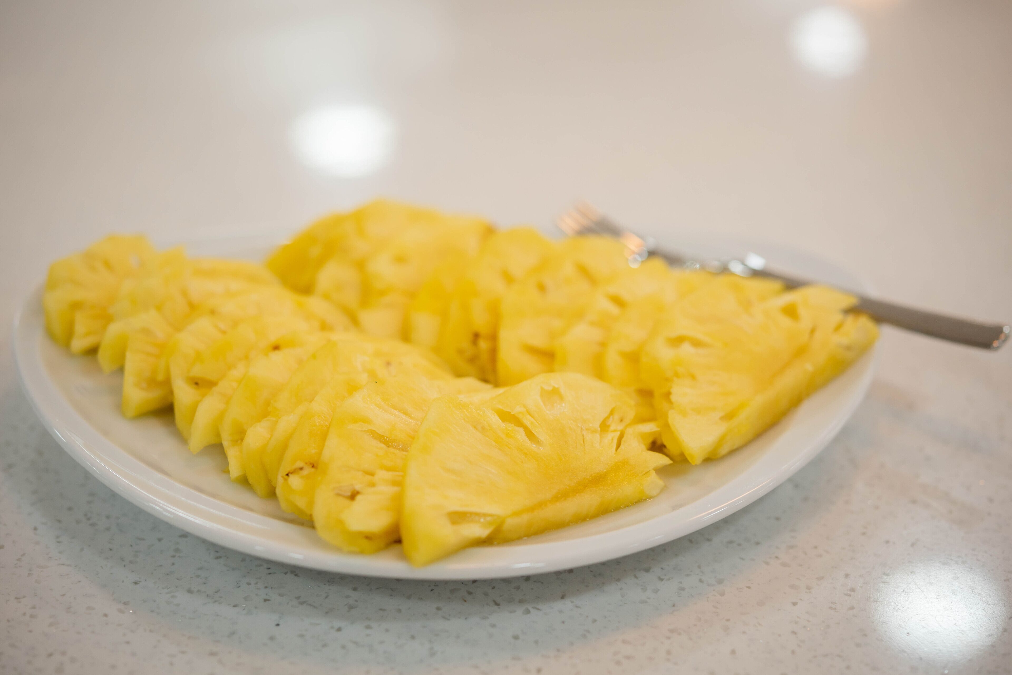 Plato blanco con rodajas de piña sobre una encimera moteada.