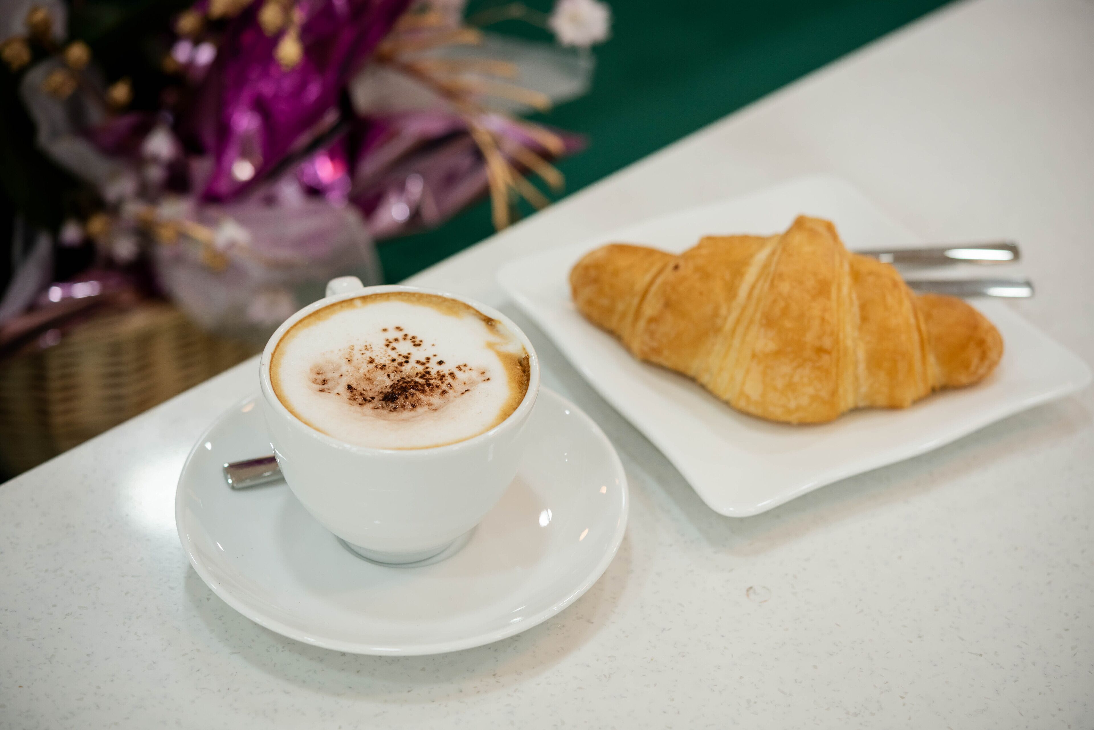 A cup of coffee with a saucer and a croissant on a white plate.