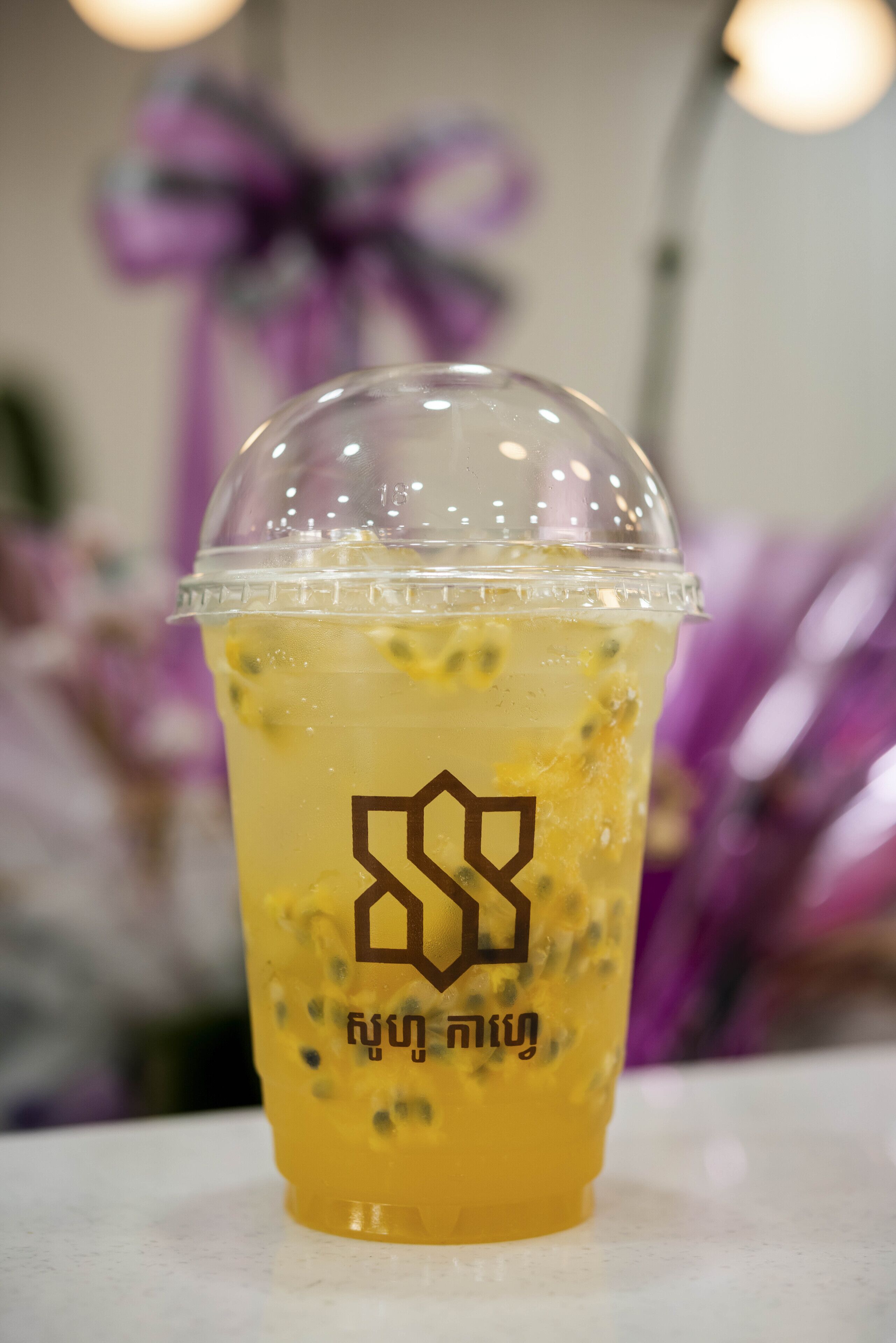 A clear plastic cup with a yellow beverage and a logo, placed on a white surface.