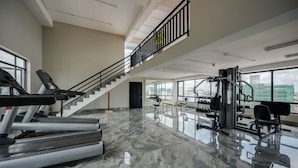 Un gimnasio amplio con cintas de correr, máquinas de pesas y una escalera que conduce a un nivel superior.