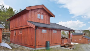 A red wooden cabin with a porch and a small deck, surrounded by a gravel path and sparse vegetation. - 2 bedroom awesome home in Nordberg (Nordberg)