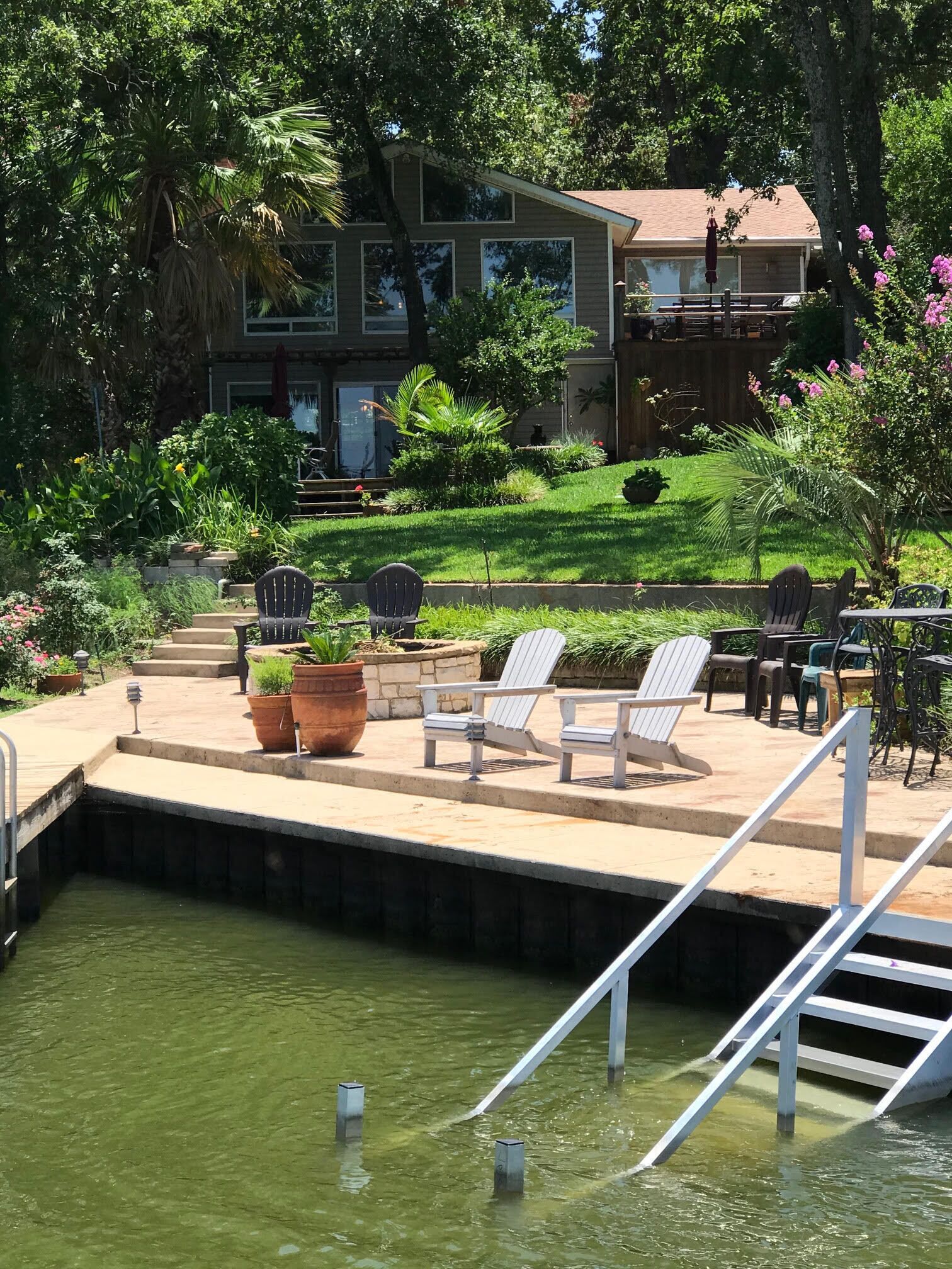 Un área junto a la piscina con plataforma de hormigón, sillas de descanso y una pequeña escalera de acceso al agua.