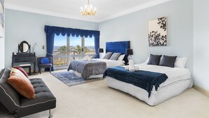 A bedroom with a large bed, a smaller bed, a vanity, a chair, and a view of the outdoors. - Razorback Dream Farmhouse: 10BR, Space & Serenity (Razorback)
