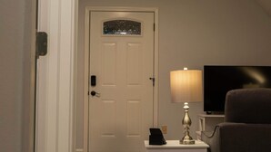 A room with a closed door, a small table with a lamp, and a television on a stand.