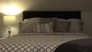 A neatly made bed with a patterned bedspread, a headboard with decorative studs, and a bedside lamp.