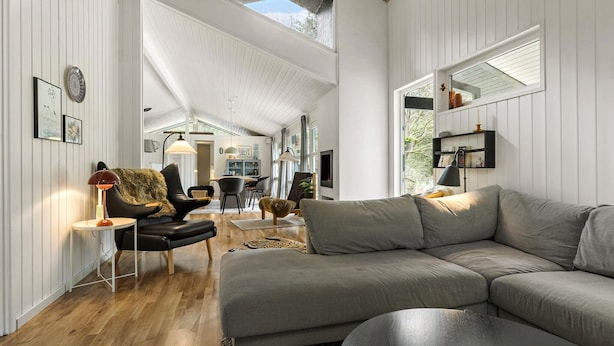 Ein geräumiges Wohnzimmer mit einem großen grauen Ecksofa, einem schwarzen Ledersessel und einem Holztisch. Im Hintergrund ist eine Essecke mit Tisch und Stühlen zu sehen.