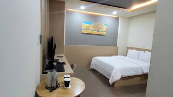 A hotel room with a bed, a desk with a coffee maker, a chair, and a painting on the wall.