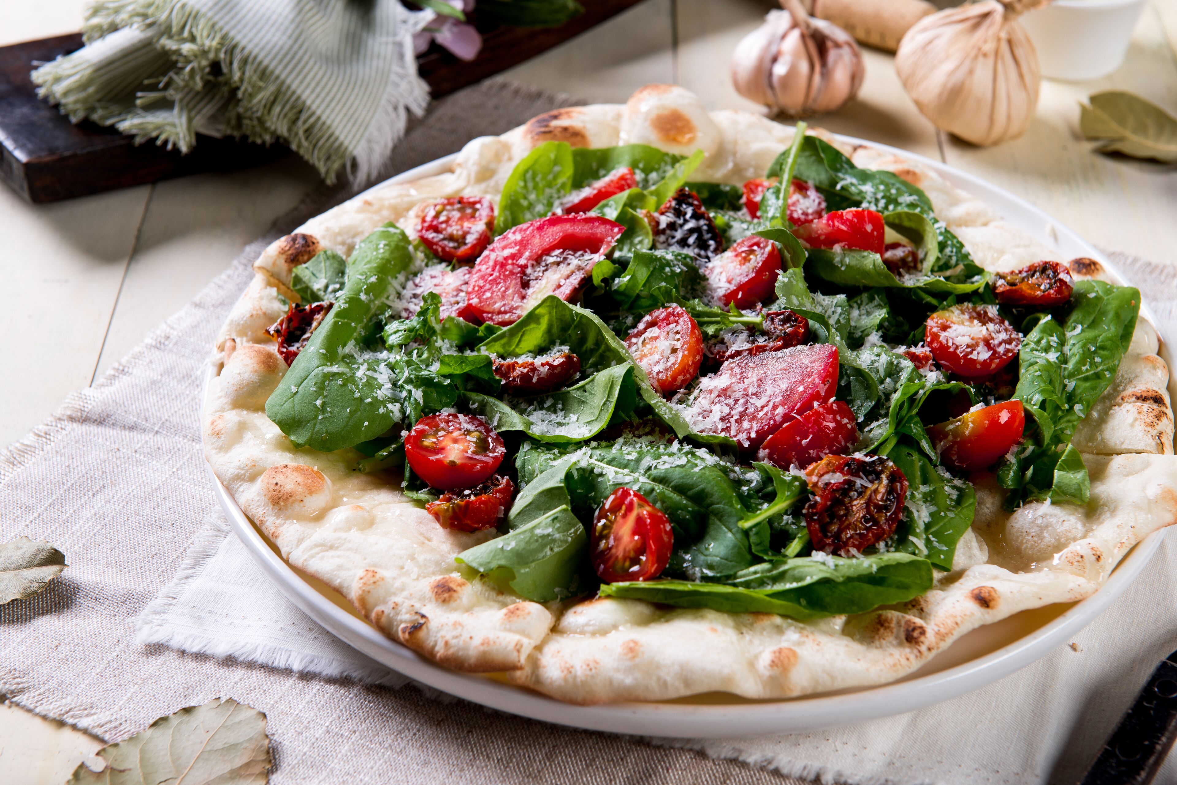 A pizza with fresh greens and tomatoes on a white plate.