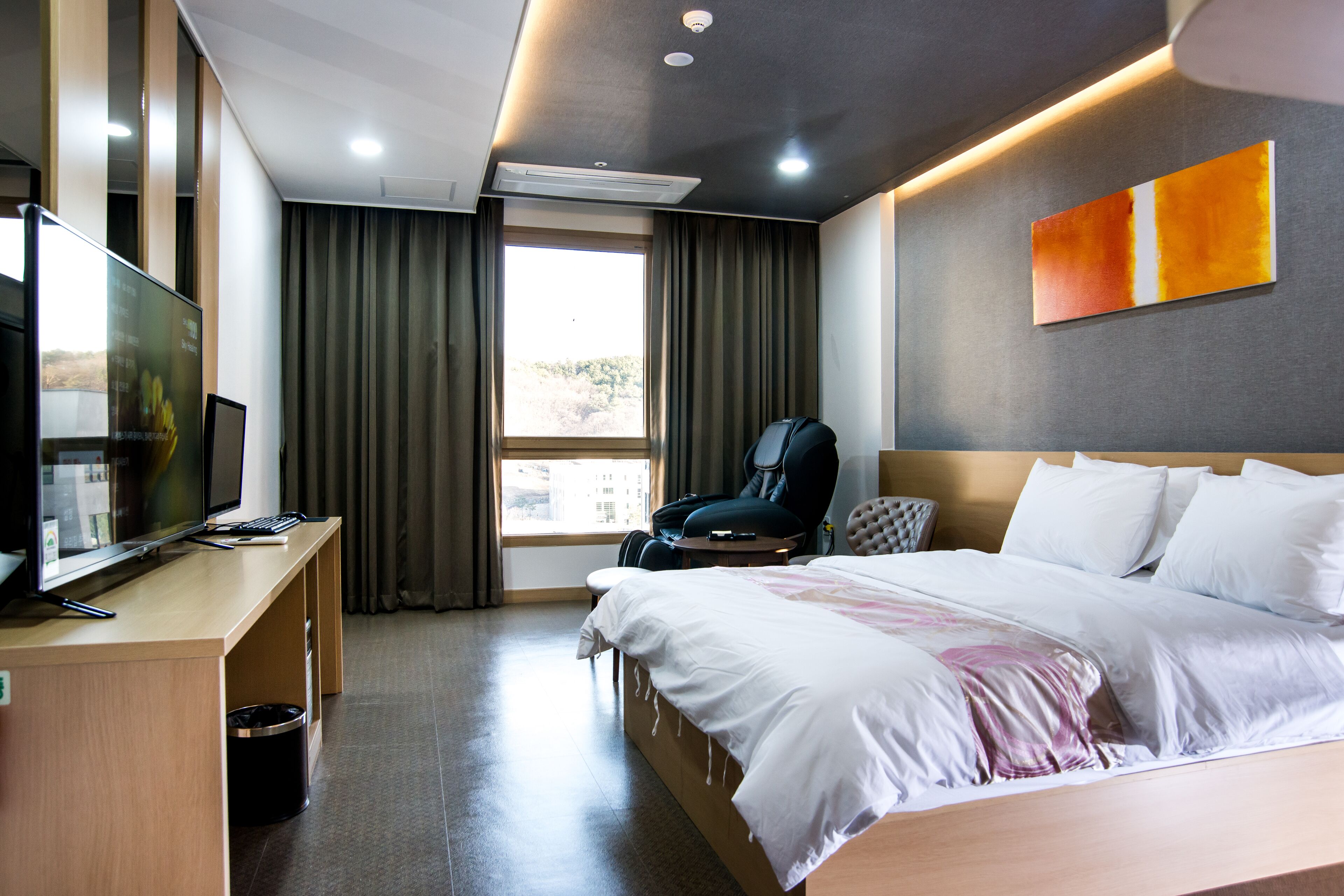 A hotel room with a bed, a desk with a computer, a chair, and a TV.