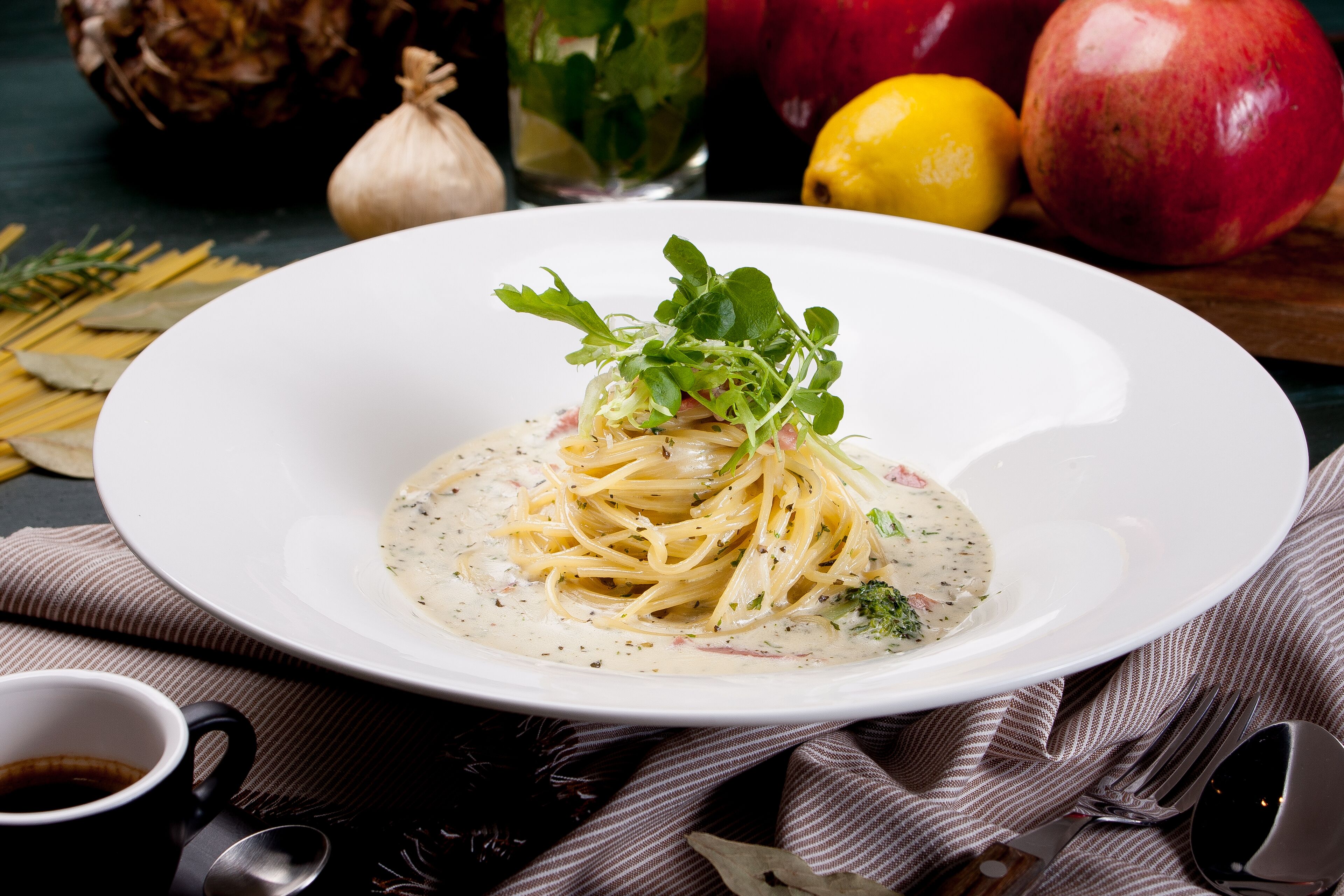 Un plato blanco con pasta y salsa cremosa, decorado con vegetales verdes, sobre un mantel oscuro.