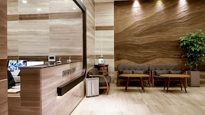 Un área de recepción con un mostrador de madera, asientos y una planta grande.