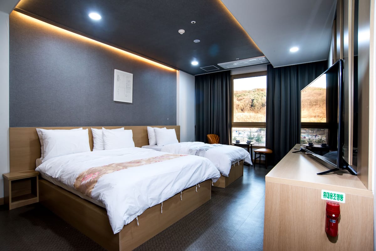 A hotel room with a large bed, bedside tables, a desk with a chair, a TV, and a window with a view.