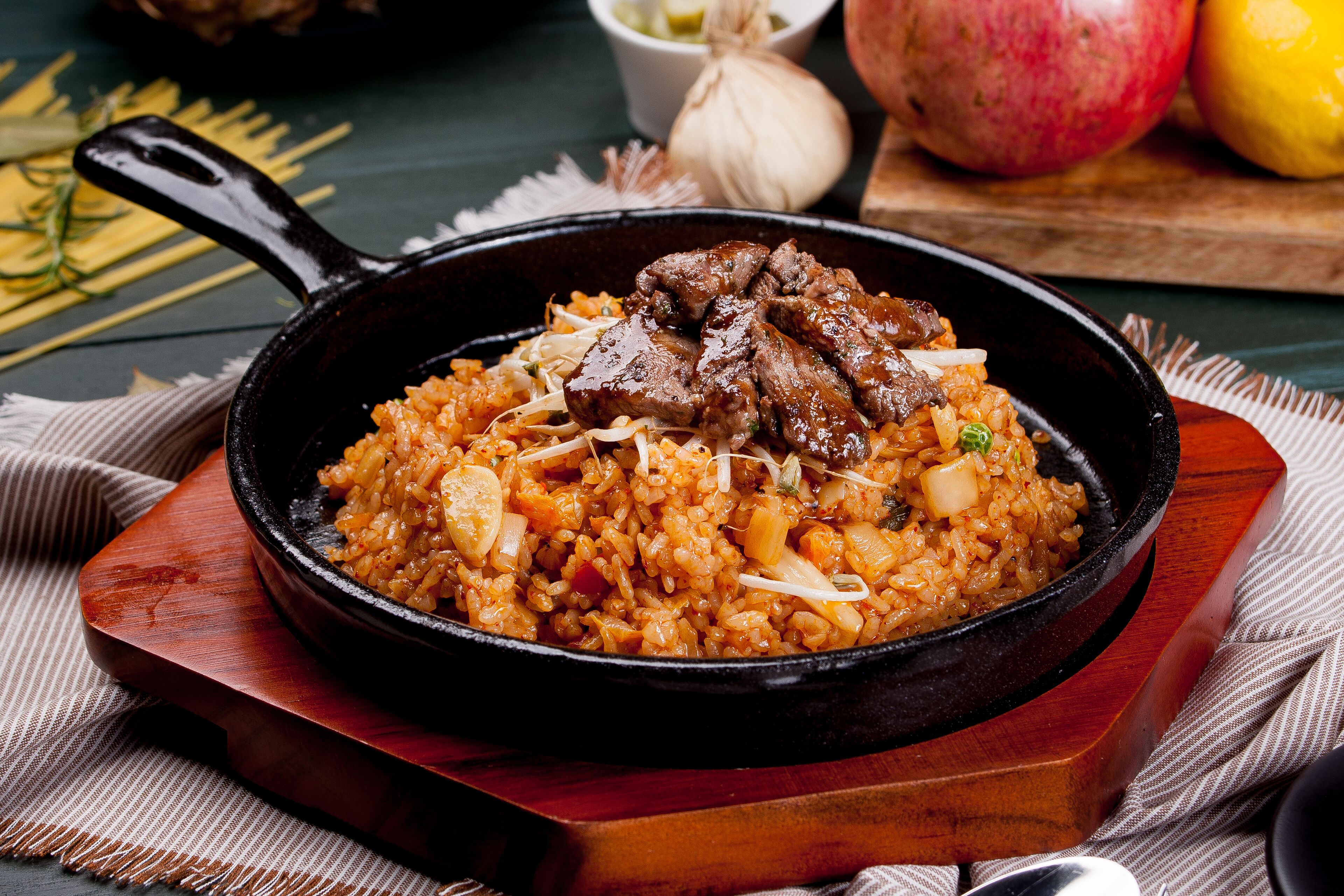 A skillet with a dish of rice and meat, placed on a wooden board.