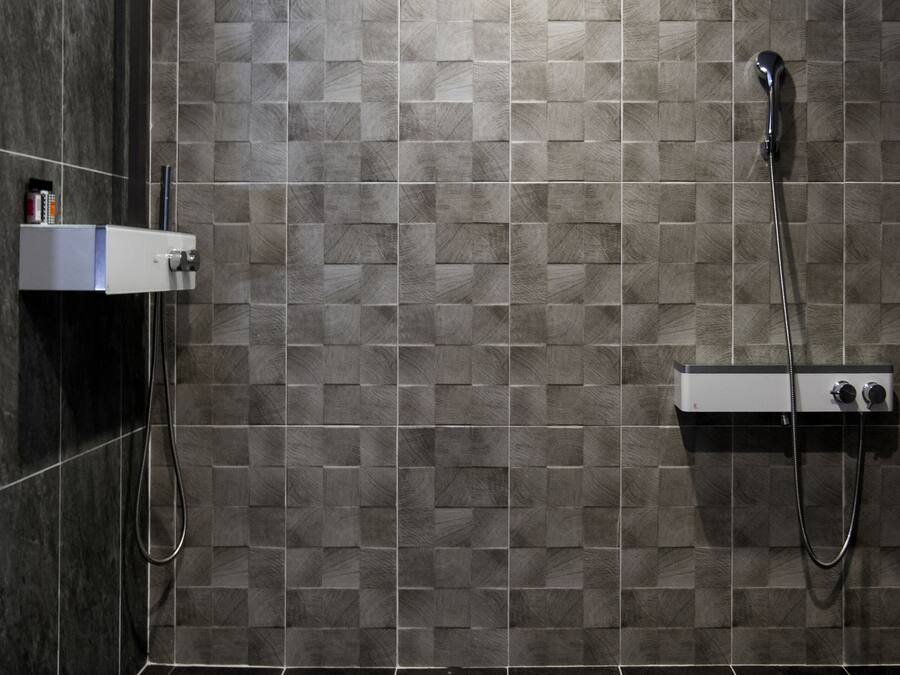 A modern shower area with a tiled wall, a handheld showerhead, and a control panel.