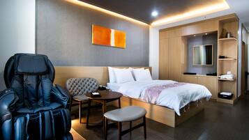 A modern hotel room with a massage chair, a small table, a bed, and a wardrobe.