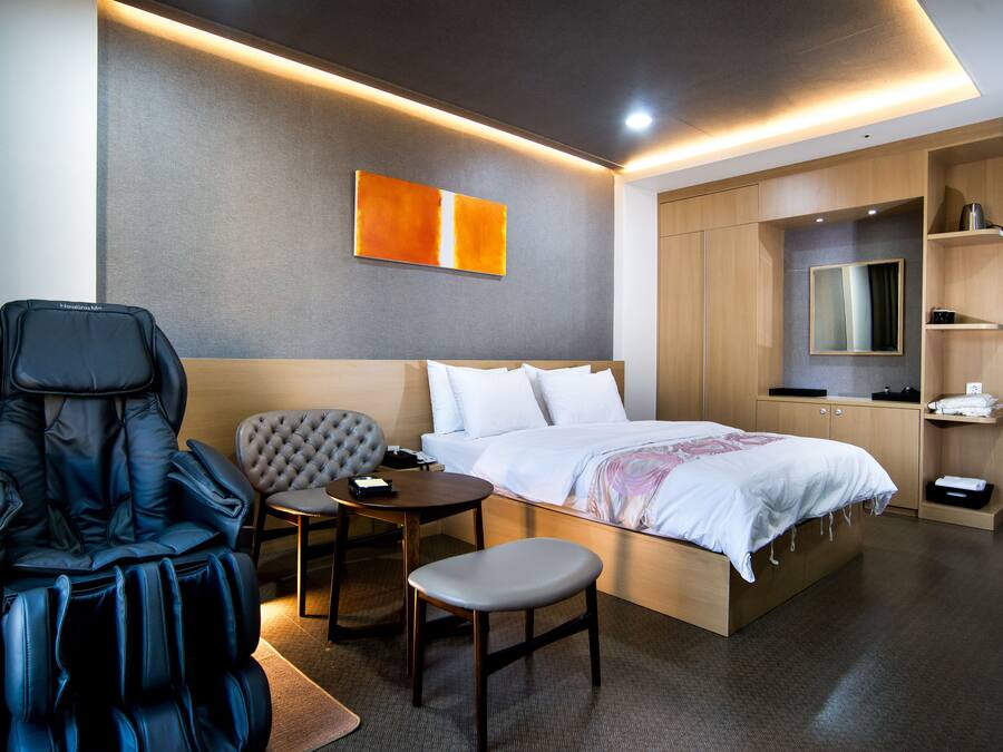 A modern hotel room with a massage chair, a small table, a bed, and a wardrobe.