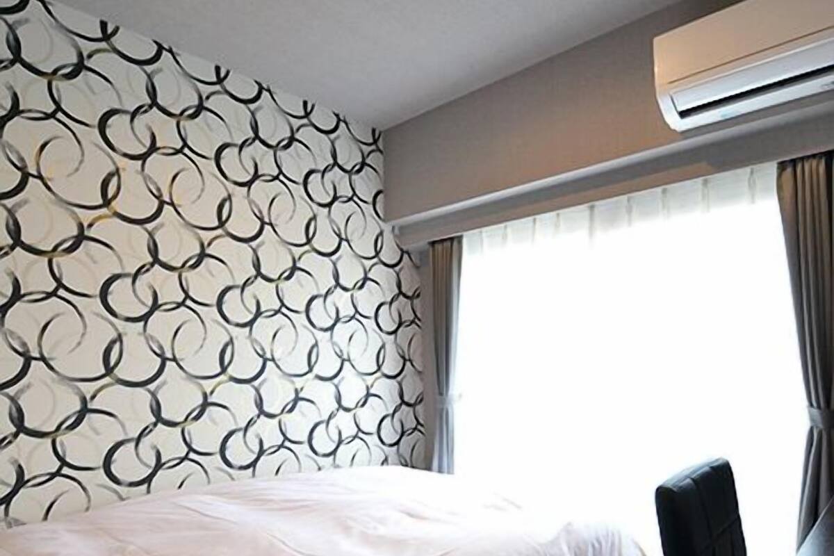 A hotel room with a patterned wall, a bed, a desk, and an air conditioning unit.