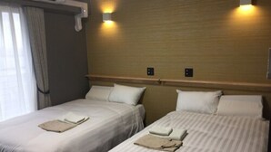 A hotel room with two beds, each with a pillow and a folded towel. There is an air conditioning unit above the window and wall-mounted lights above the beds. - Omura Station Hotel Nagasaki Airport (Omura)