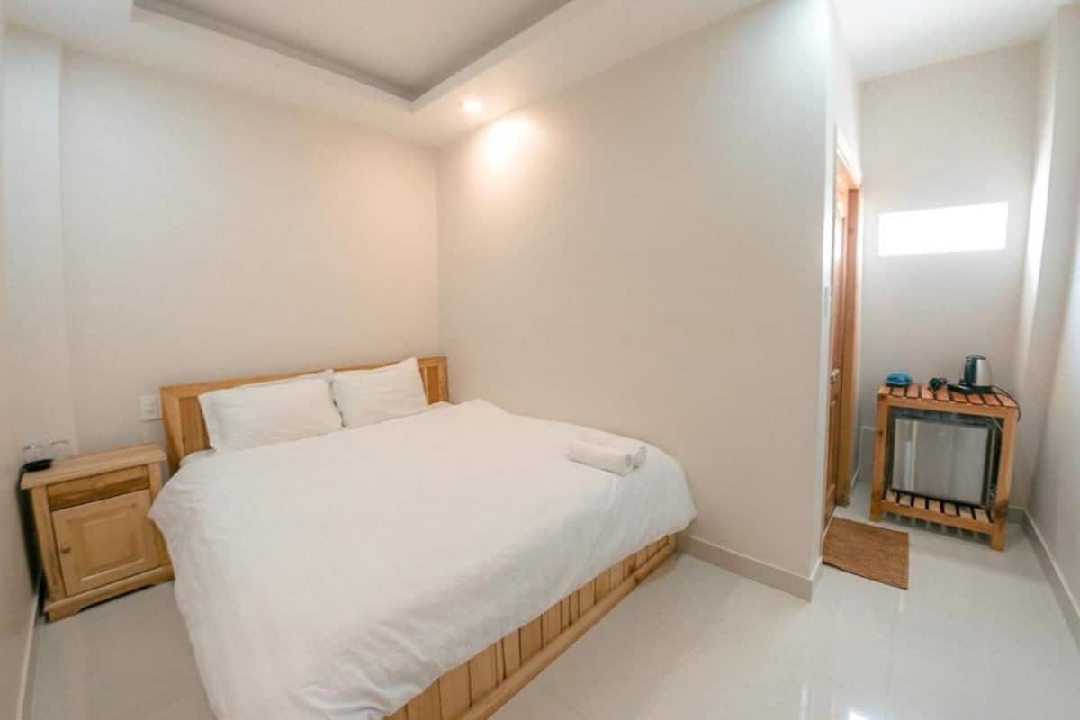 A bedroom with a bed, nightstands, a small heater, and a window.