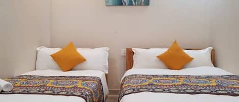 A hotel room with two single beds, each with a patterned bedspread and a white pillow.