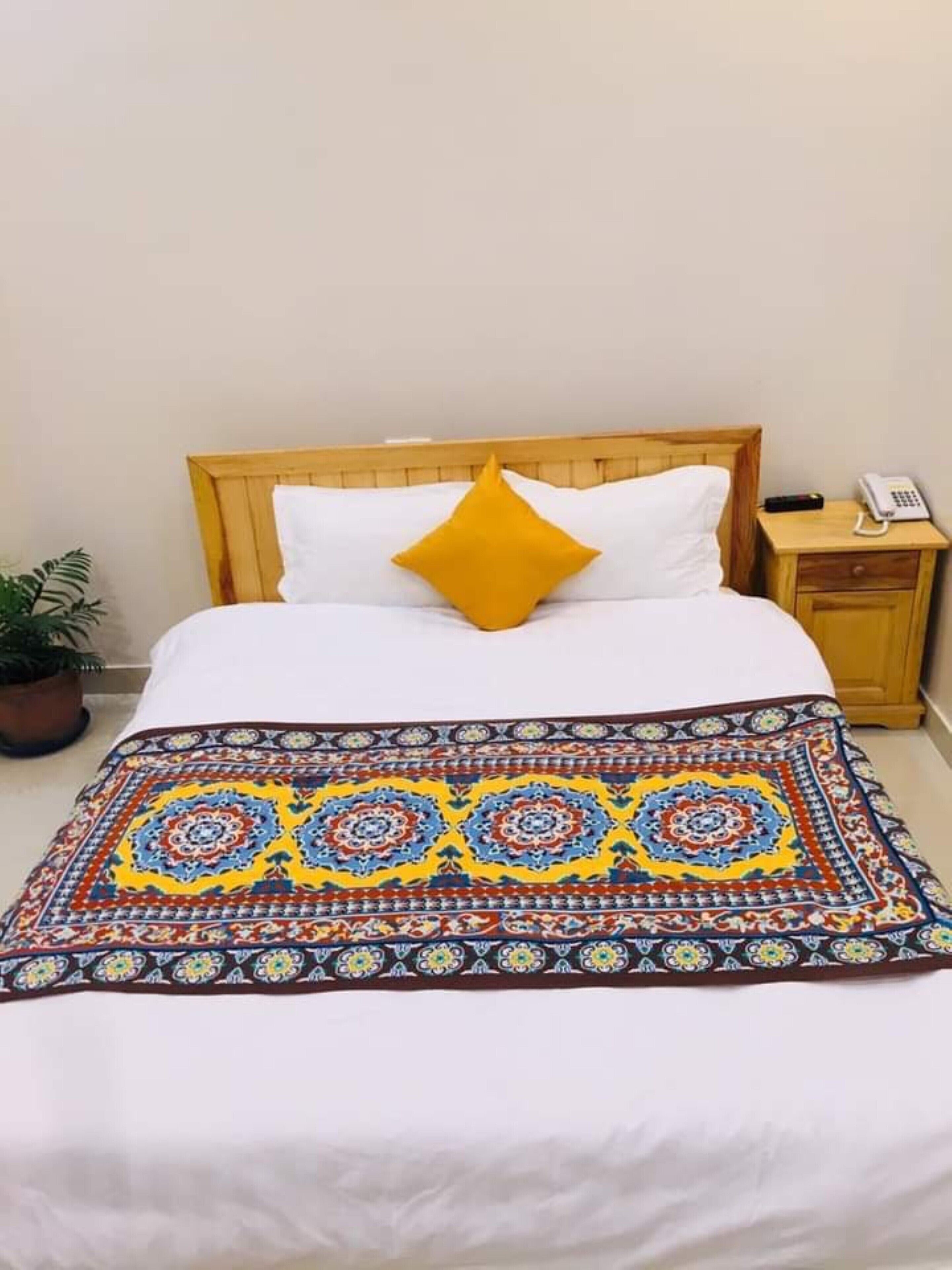 A bed with a wooden headboard, white bedding, a single yellow pillow, and a patterned throw blanket.