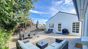 Un patio con mobiliario exterior, una parrilla y un edificio blanco con ventanas.