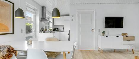 Et moderne køkken med hvide skabe, hængende lamper og et spiseområde med hvide stole og en blød måtte.