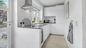 Una cocina moderna con armarios blancos, una campana extractora de acero inoxidable, un horno empotrado y un ventanal con vistas a un jardín.