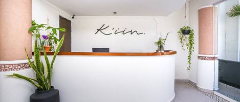 Un comptoir d’accueil avec une enseigne indiquant « Kiin ». De part et d’autre du comptoir, on trouve des plantes en pot.