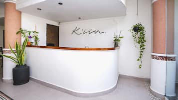 A reception desk with the name 'Kim' in cursive on the wall, surrounded by potted plants and a tiled floor.