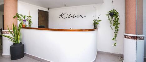 A reception desk with the name 'Kim' in cursive on the wall, surrounded by potted plants and a tiled floor.