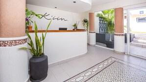A reception area with a white wall, a wooden reception desk, and several potted plants. - Hotel Kiin Cozumel (Cozumel)