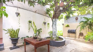 A courtyard with a wooden table, potted plants, hanging planters, a grill, and a tree. - Hotel Kiin Cozumel (Cozumel)