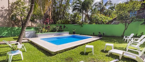 A swimming pool surrounded by green grass, white lounge chairs, and palm trees.