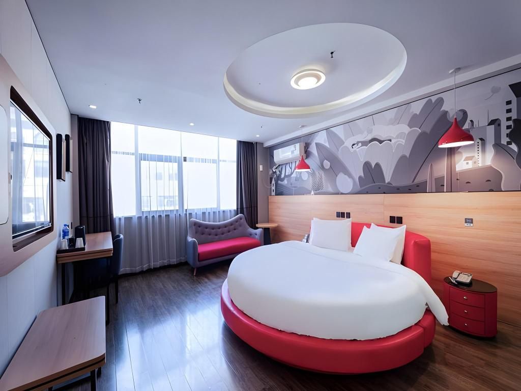 A modern hotel room with a large bed, a desk, a chair, and a sofa.