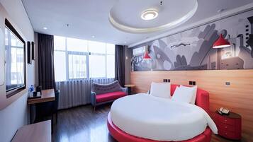 A modern hotel room with a large bed, a desk, a chair, and a sofa.