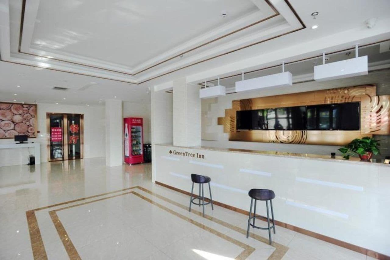 A modern hotel lobby with a reception desk, bar area, and a large TV screen.