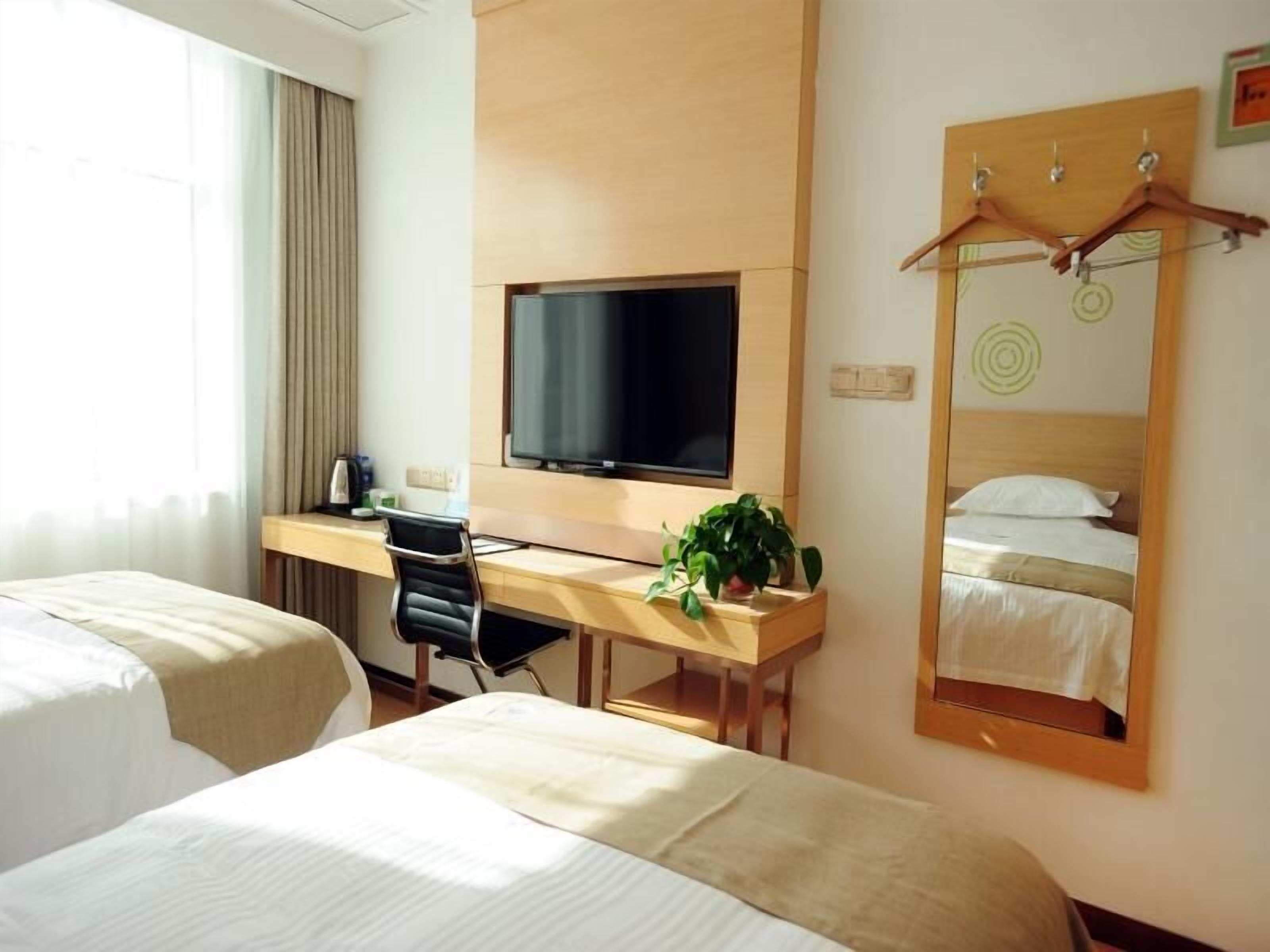 A hotel room with two beds, a desk with a TV, a mirror, and a plant.