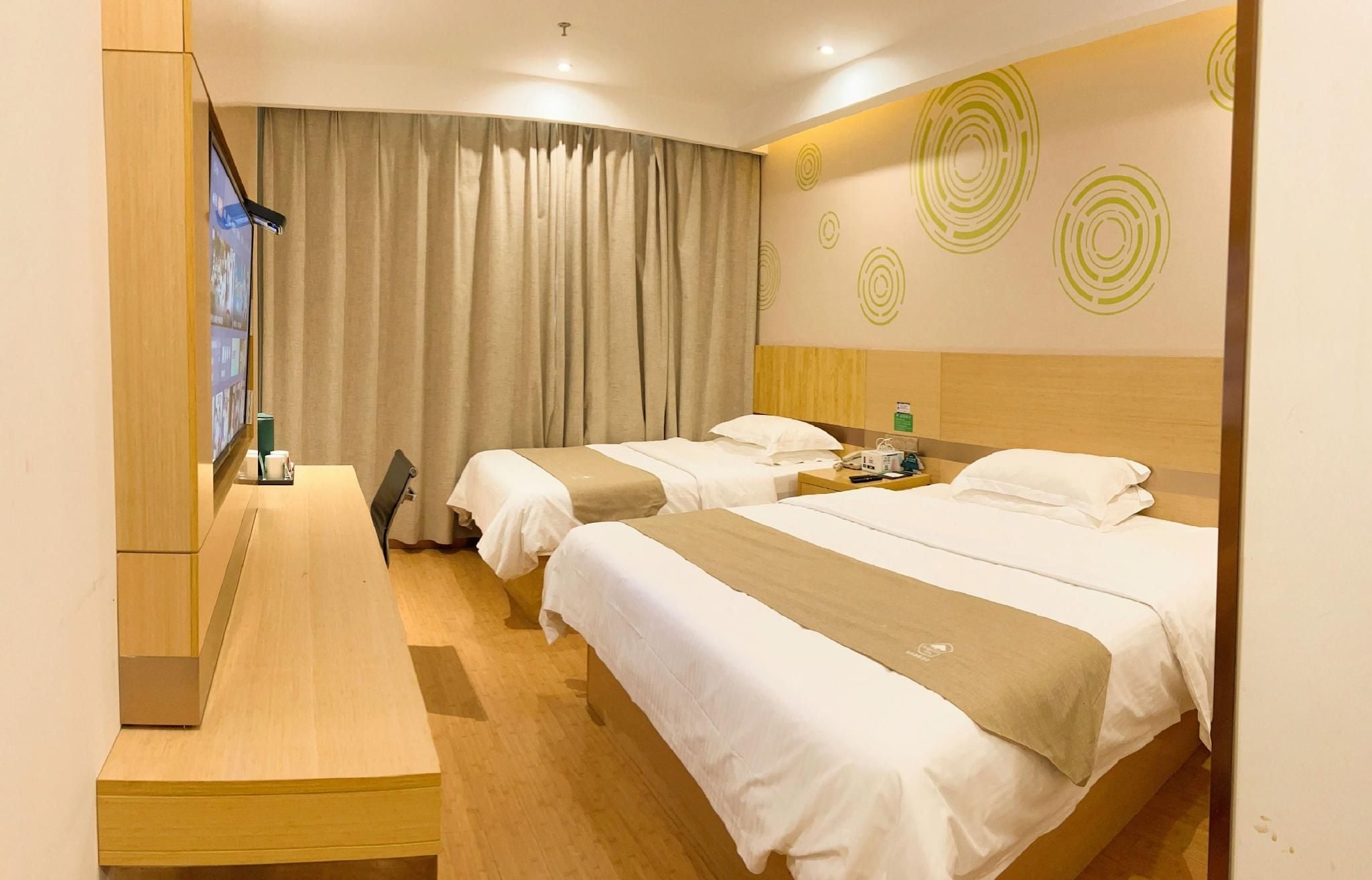A hotel room with two beds, a desk, and a large window with curtains.