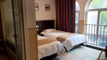 Habitación de hotel con dos camas, un ventanal con cortinas y vistas al exterior.