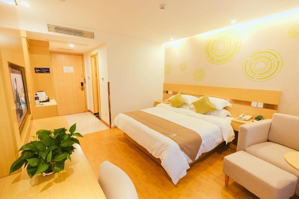 Habitación de hotel con cama, mesita de noche, silla y una planta en maceta.