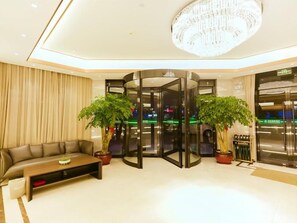 A lobby with a sofa, a coffee table, two potted plants, a chandelier, and a revolving door. - Greentree Inn Haining Chang an University Town (Jiaxing)
