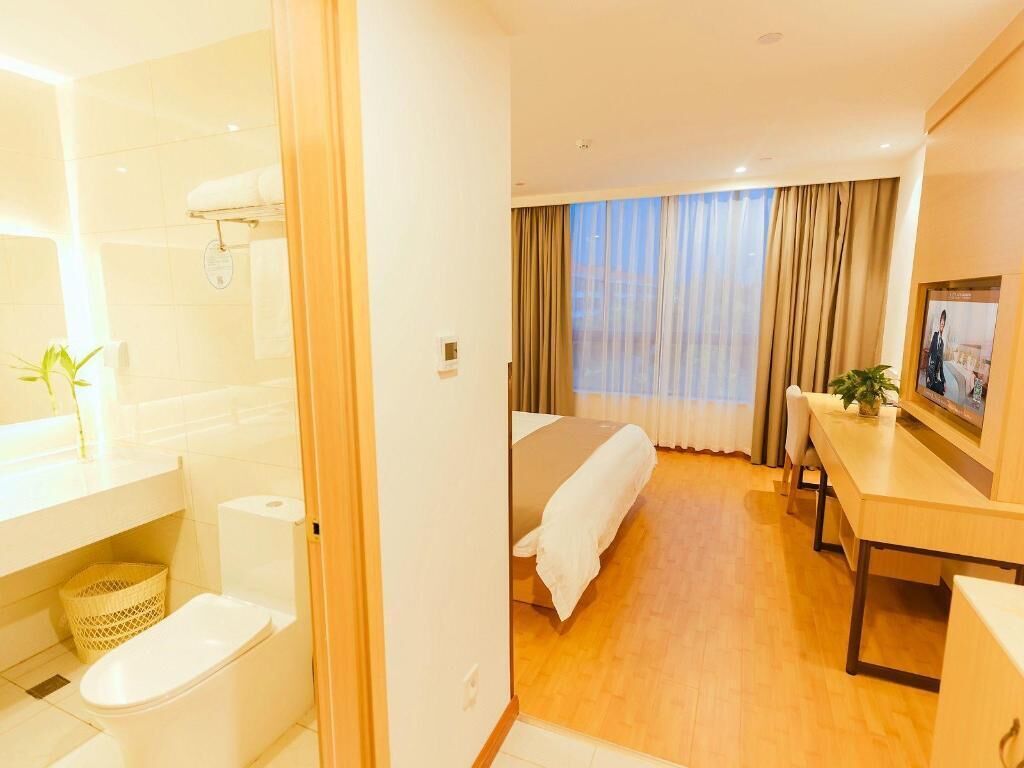 Ein Hotelzimmer mit Bett, Schreibtisch, Fernseher, Badezimmer mit Toilette und Waschbecken sowie einem Fenster mit Vorhängen.