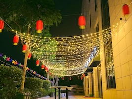 Un espacio al aire libre con luces colgantes y faroles rojos, un banco y un edificio con fachada de azulejos.