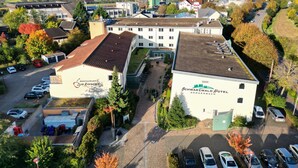 A hotel with a flat roof, surrounded by parked cars and trees.
