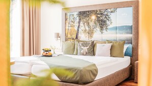 A modern bedroom with a large bed, a headboard with a nature-themed mural, and a bedside table with a lamp and a fruit bowl.