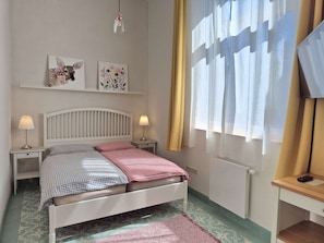 A bedroom with a bed, bedside lamps, a radiator, a desk, and a window with curtains. - BLUMENWIESE at the Grombach train station — beautiful, small, and cozy (Bad Rappenau)