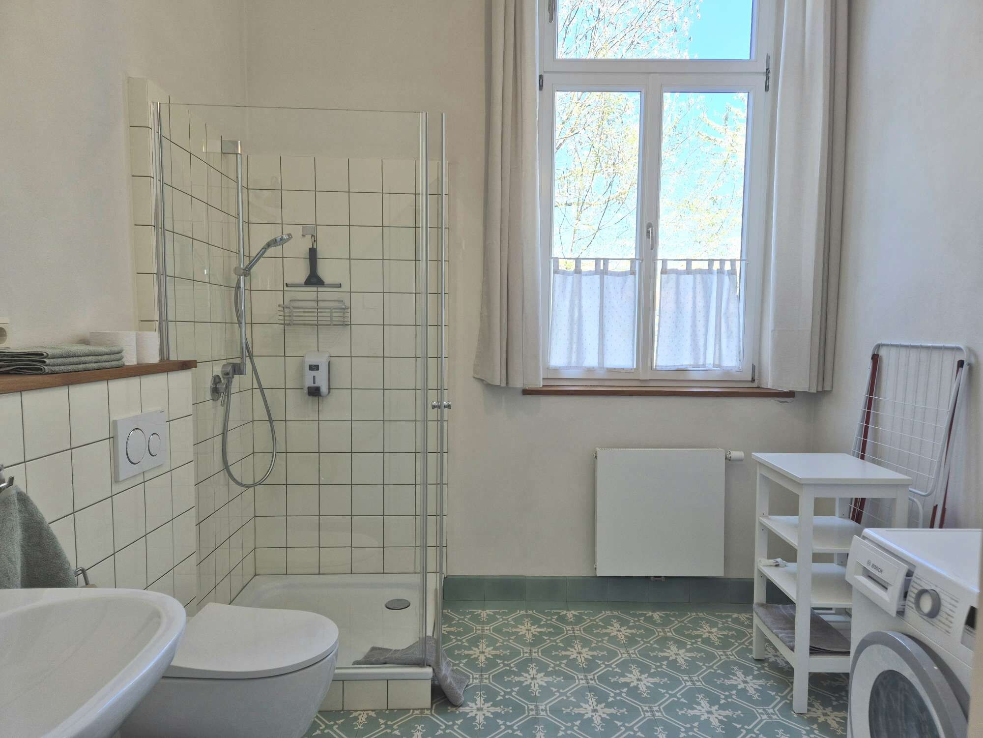 A bathroom with a shower, toilet, and a window with a view of trees.