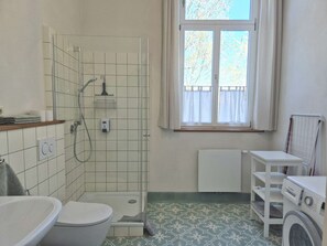 A bathroom with a shower, toilet, and a window with a view of trees.
